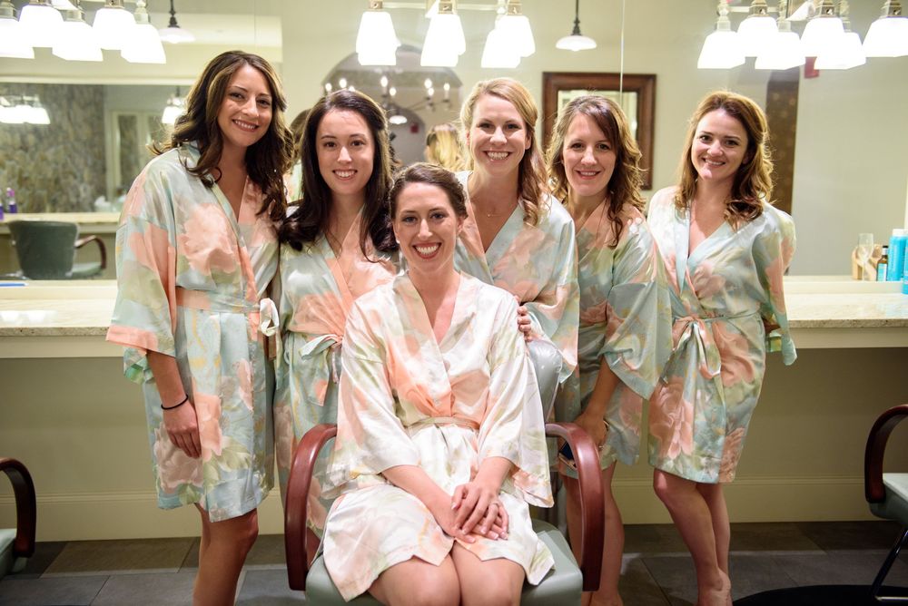 Wedding party wearing matching floral robes posing together in bright room.