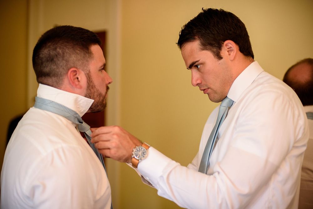 Groomsmen in white shirts helping each other prepare for wedding ceremony.
