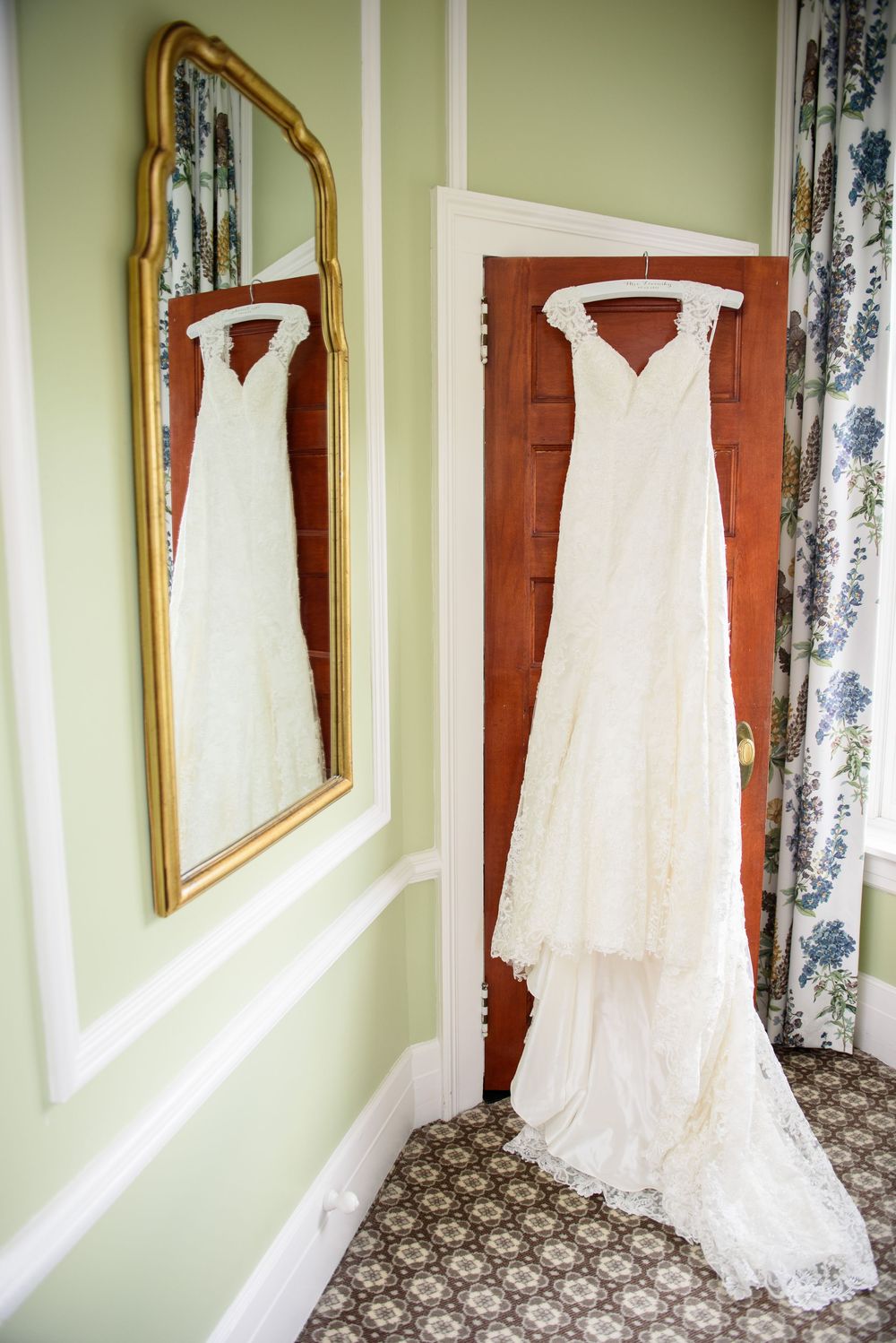 Elegant white lace wedding dress displayed hanging in multiple angles against light green walls and floral curtains.