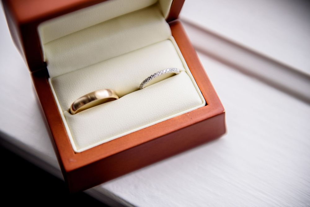 Gold wedding bands displayed in brown leather jewelry boxes on white surface.