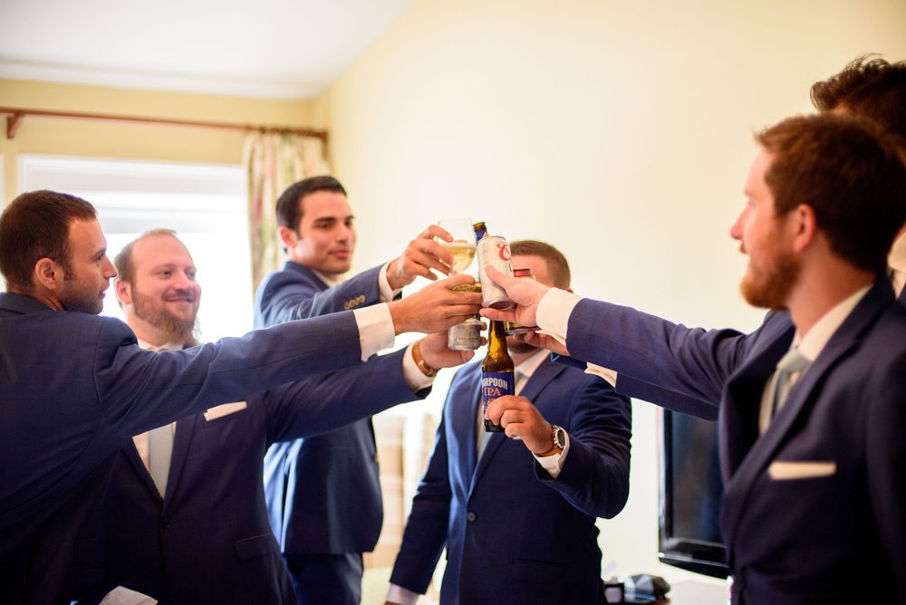 Groomsmen sharing laughs and casual moments while getting dressed for wedding.