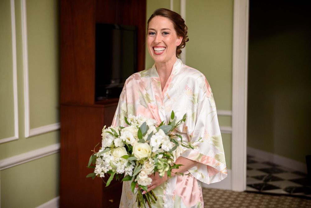 Bride in floral robe holding white bouquet during wedding morning preparations.