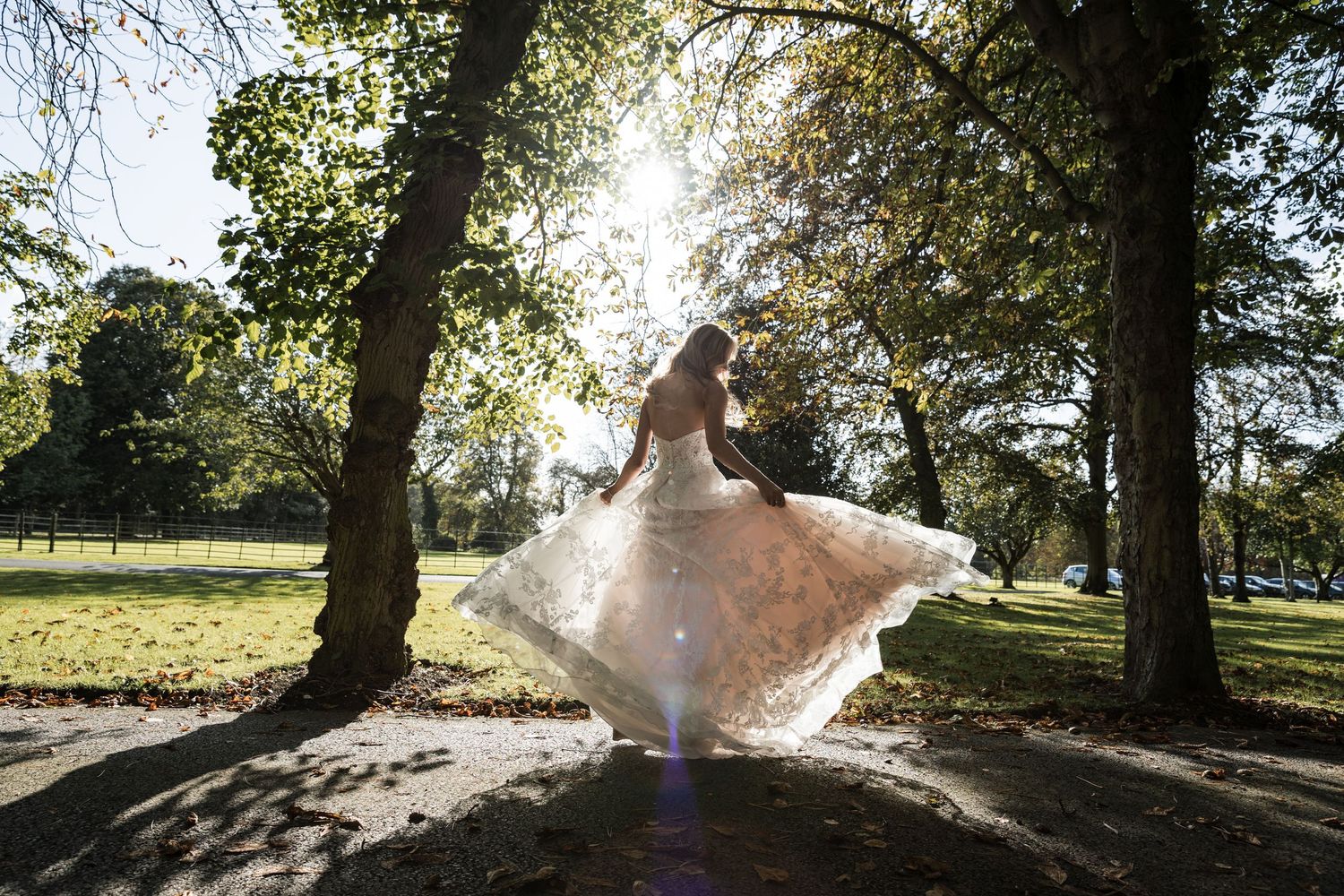 Bride’s flowing white wedding dress billowing in the breeze as sunlight streams through the trees at Kelham House grounds