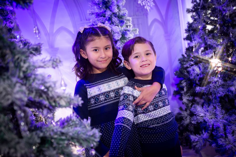 Children wearing winter sweaters pose together against a purple backdrop with glowing snowflake decorations.