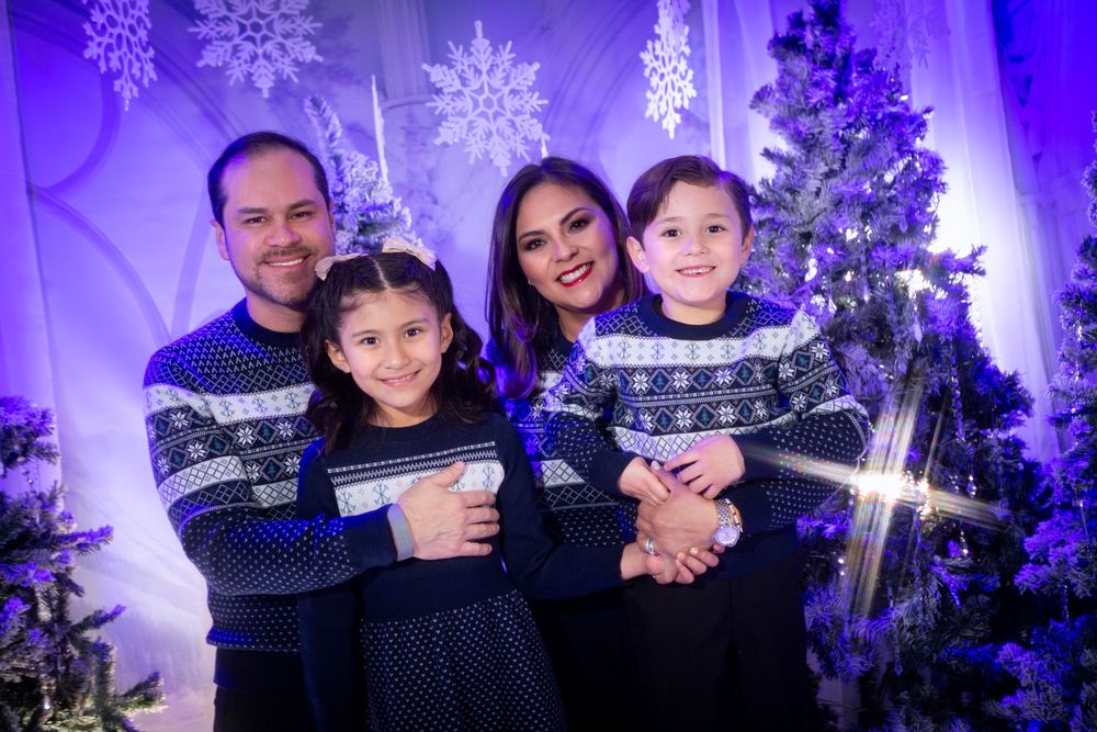 A family poses in front of a purple-lit Christmas tree and winter holiday decorations at a festive gathering.