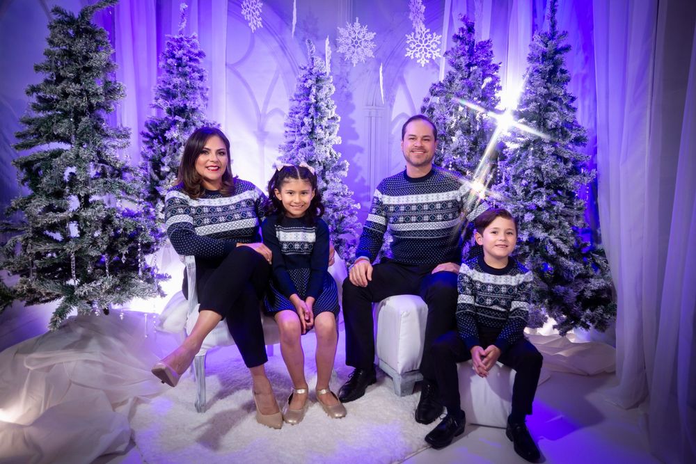 A winter wonderland photo session with people posing in front of illuminated white trees and purple lighting.