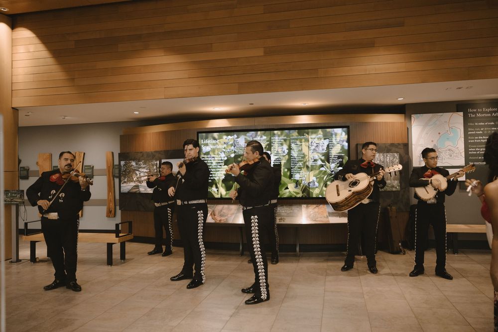 Mariachi band in traditional charro suits performing indoors at a modern venue with wood ceiling.