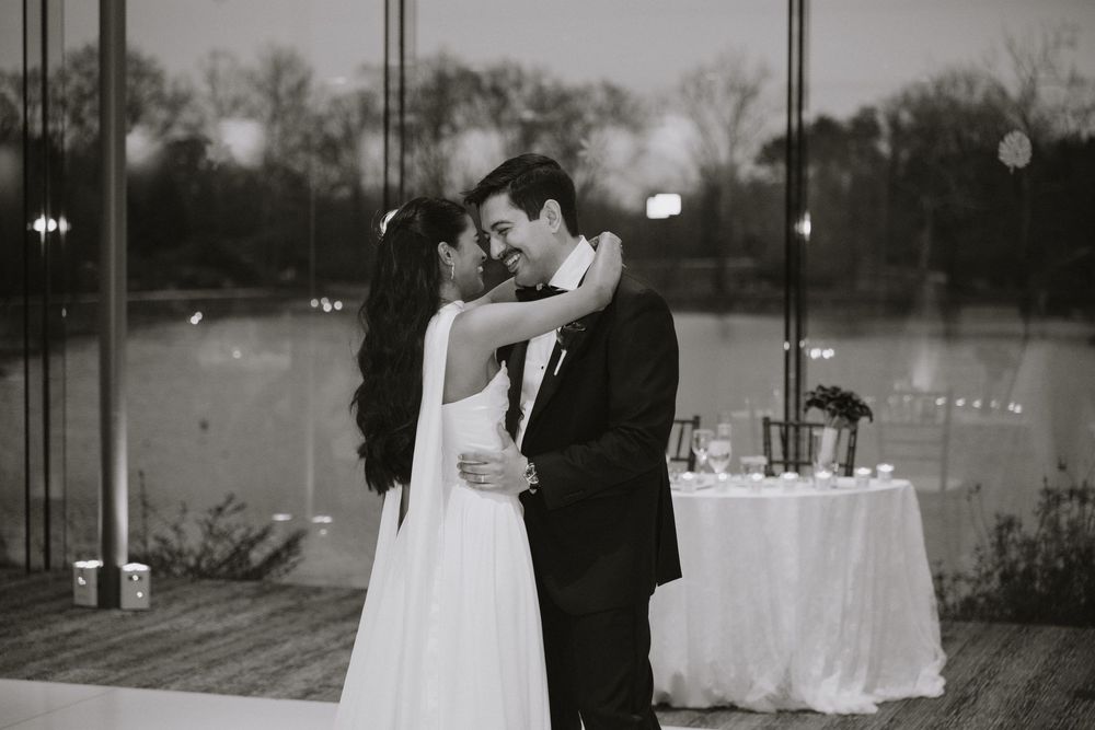 Black and white photo of a bride and groom sharing a romantic first dance kiss at their elegant waterfront wedding reception.