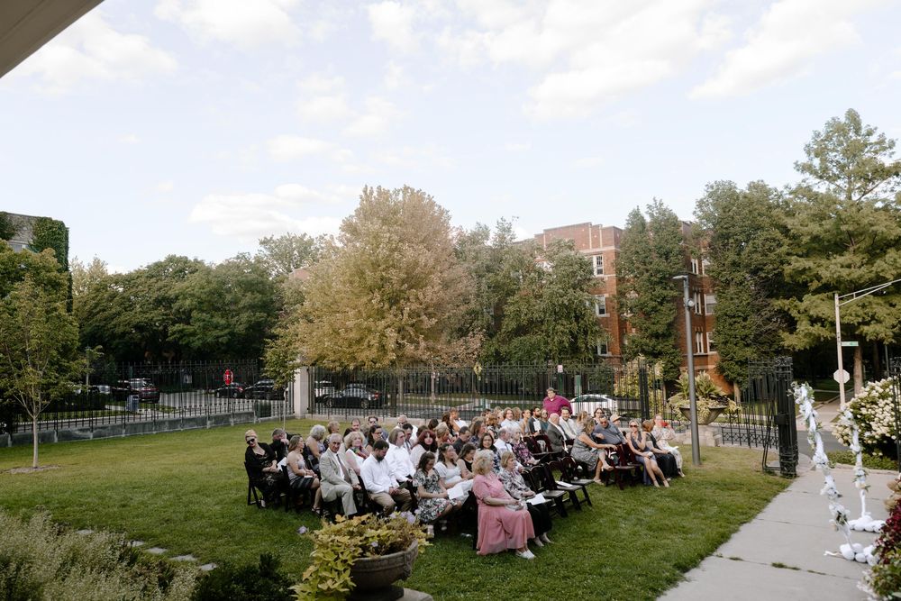 Outdoor wedding ceremony setup with rows of white chairs on a grassy lawn surrounded by trees.