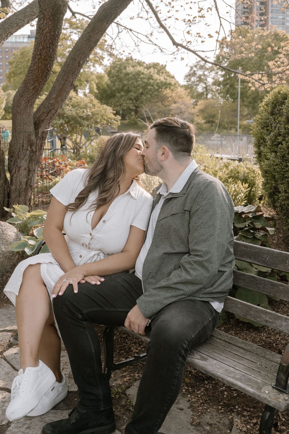 A romantic couple shares tender moments while sitting on a wooden bench in an autumn park setting.