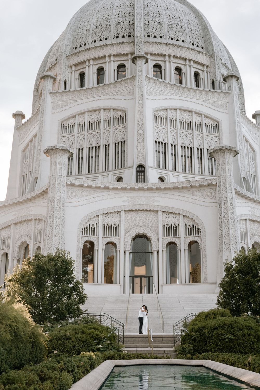 Majestic white Baha'i Temple architecture with reflecting pool and landscaped grounds on a cloudy day.