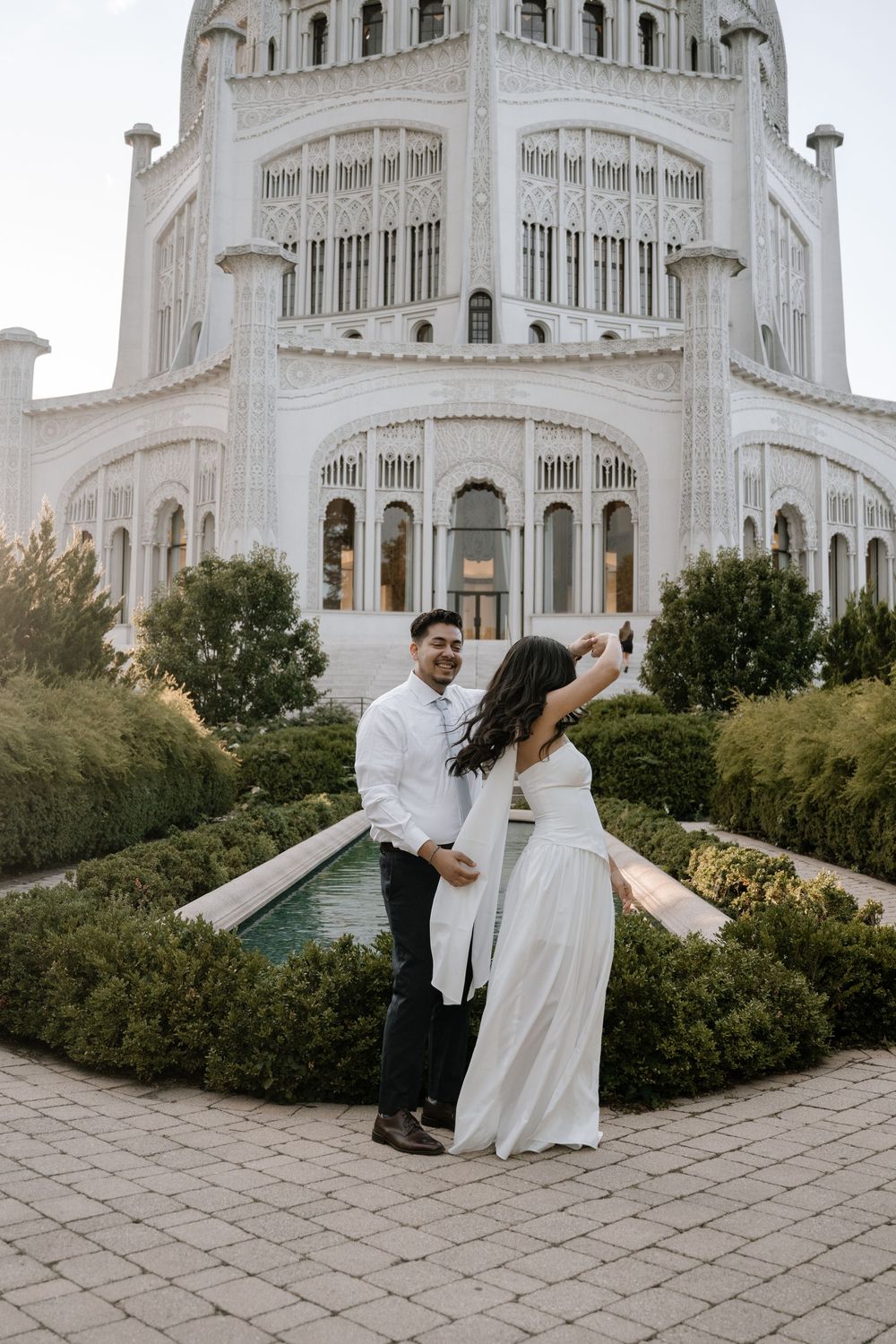 A couple in white attire shares a romantic moment in front of the majestic Baha'i House of Worship in Chicago.