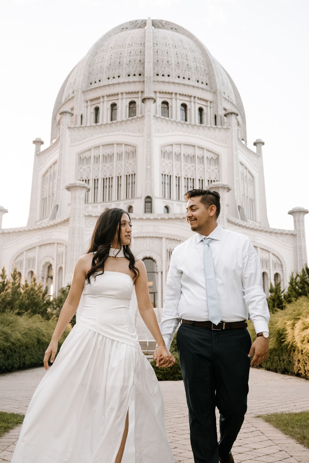 A couple in wedding attire holds hands while walking in front of the Baha'i Temple in Wilmette, Illinois.