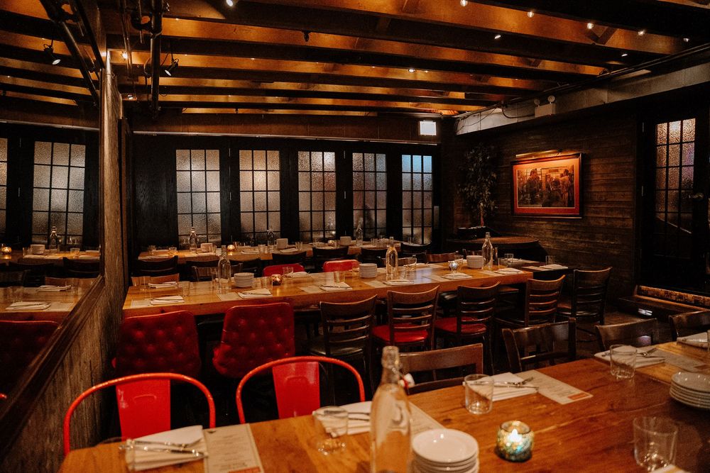 Rustic restaurant interior with wooden tables, red metal chairs, and exposed beams in warm ambient lighting.