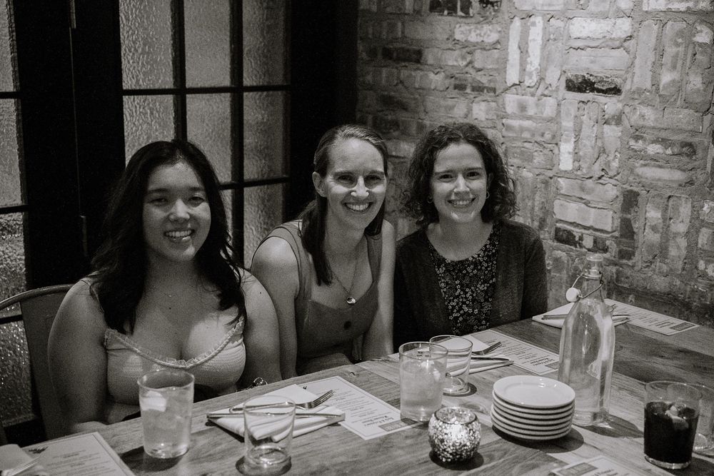 Three friends share a meal together at a restaurant table with stone walls visible in the background.