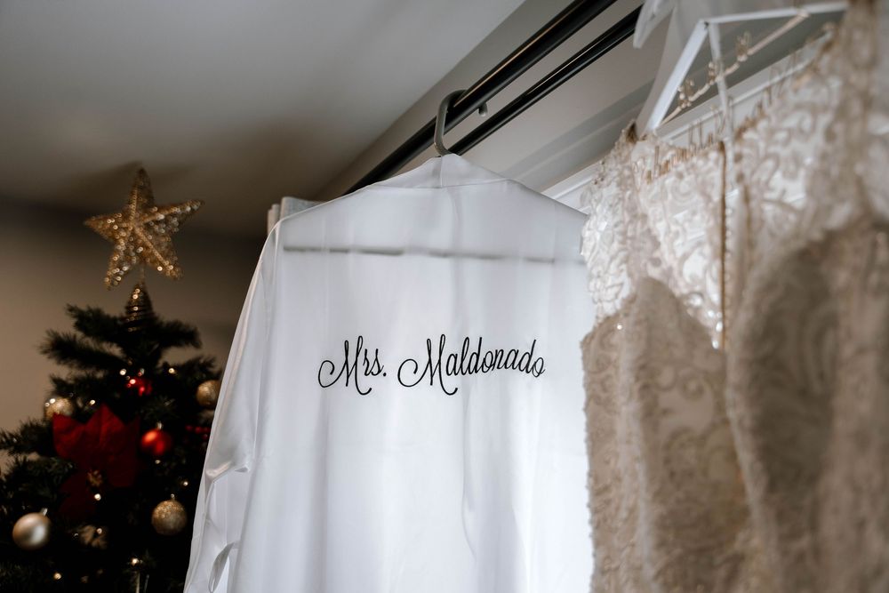 Personalized Mrs. Maldonado white bridal robe hanging near a Christmas tree and lace wedding dress.