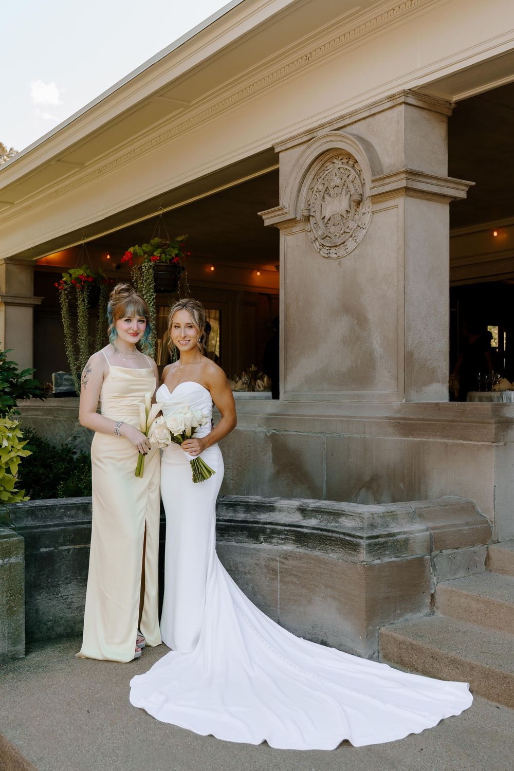 Two people in formal attire stand together in front of a stone building with elegant architecture.