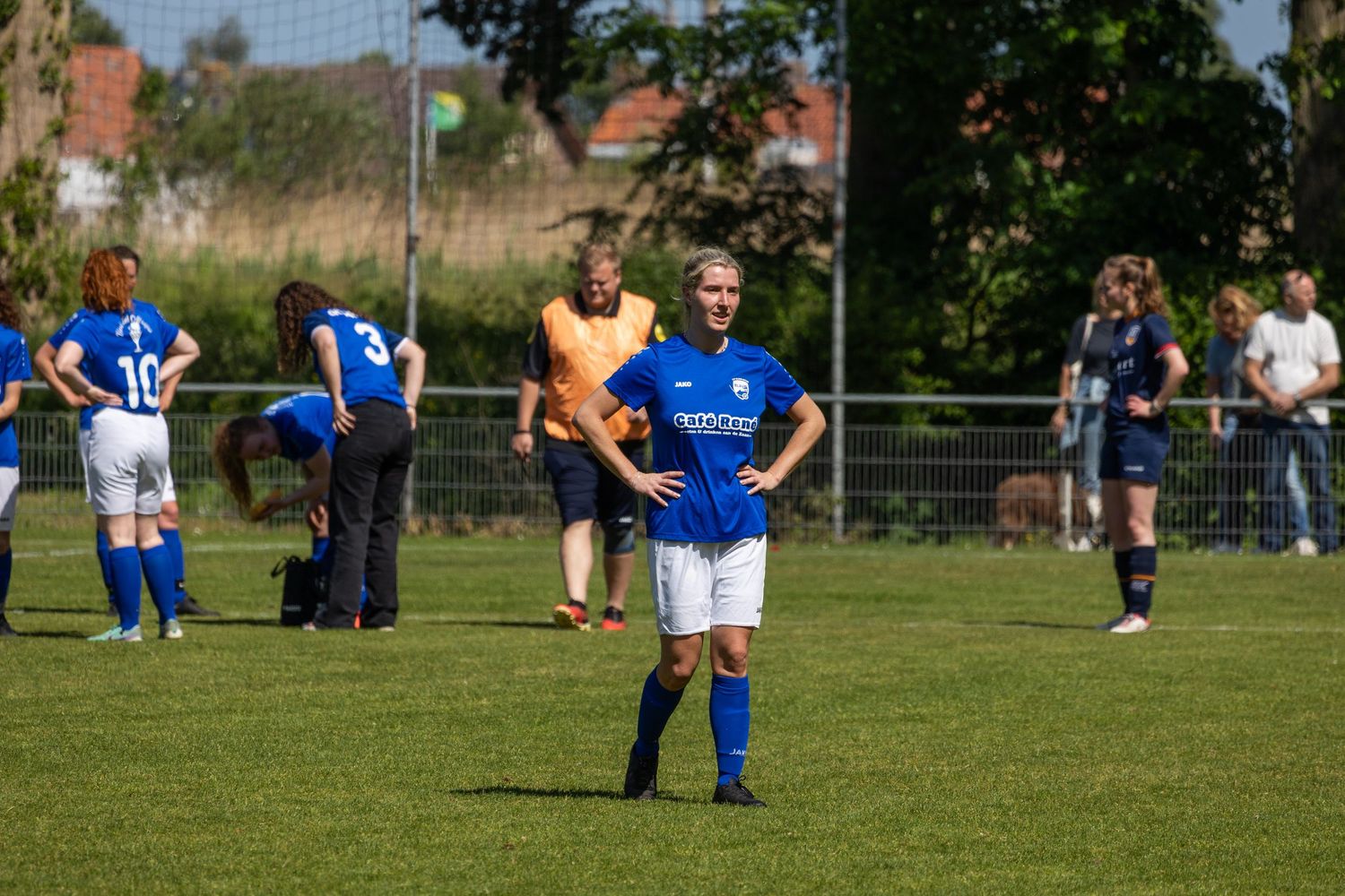 Soccer players in blue jerseys and black shorts spread across a sunny grass field during a match.