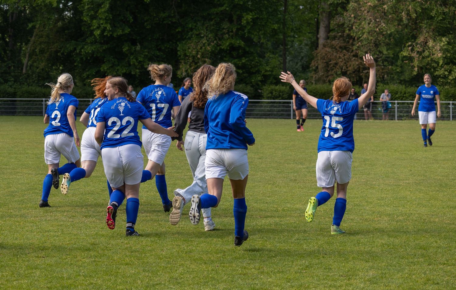 Soccer players in blue jerseys celebrate together by running and jumping on a grass field during a match.