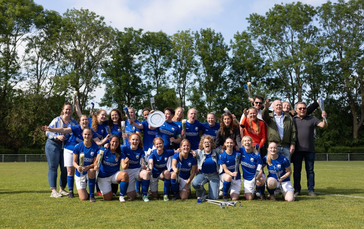 Large group of soccer players in blue uniforms posing together on a grassy field for a team photo.