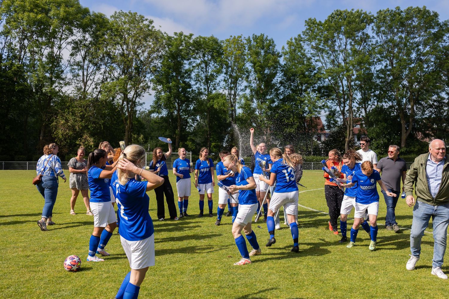 Children in blue and white uniforms practicing soccer drills together on a sunny grassy field.