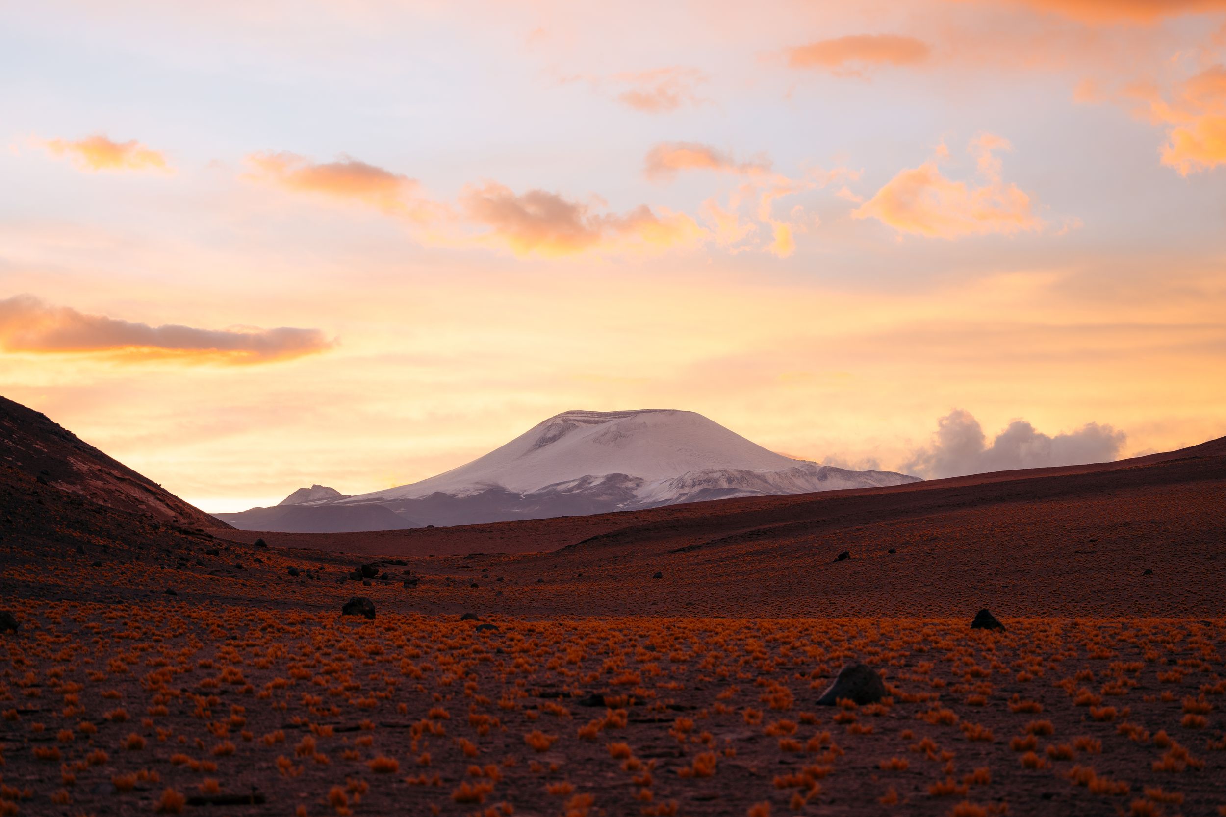 Panoramic mountain landscape at sunset with orange and purple sky reflecting off mountains in silhouette.