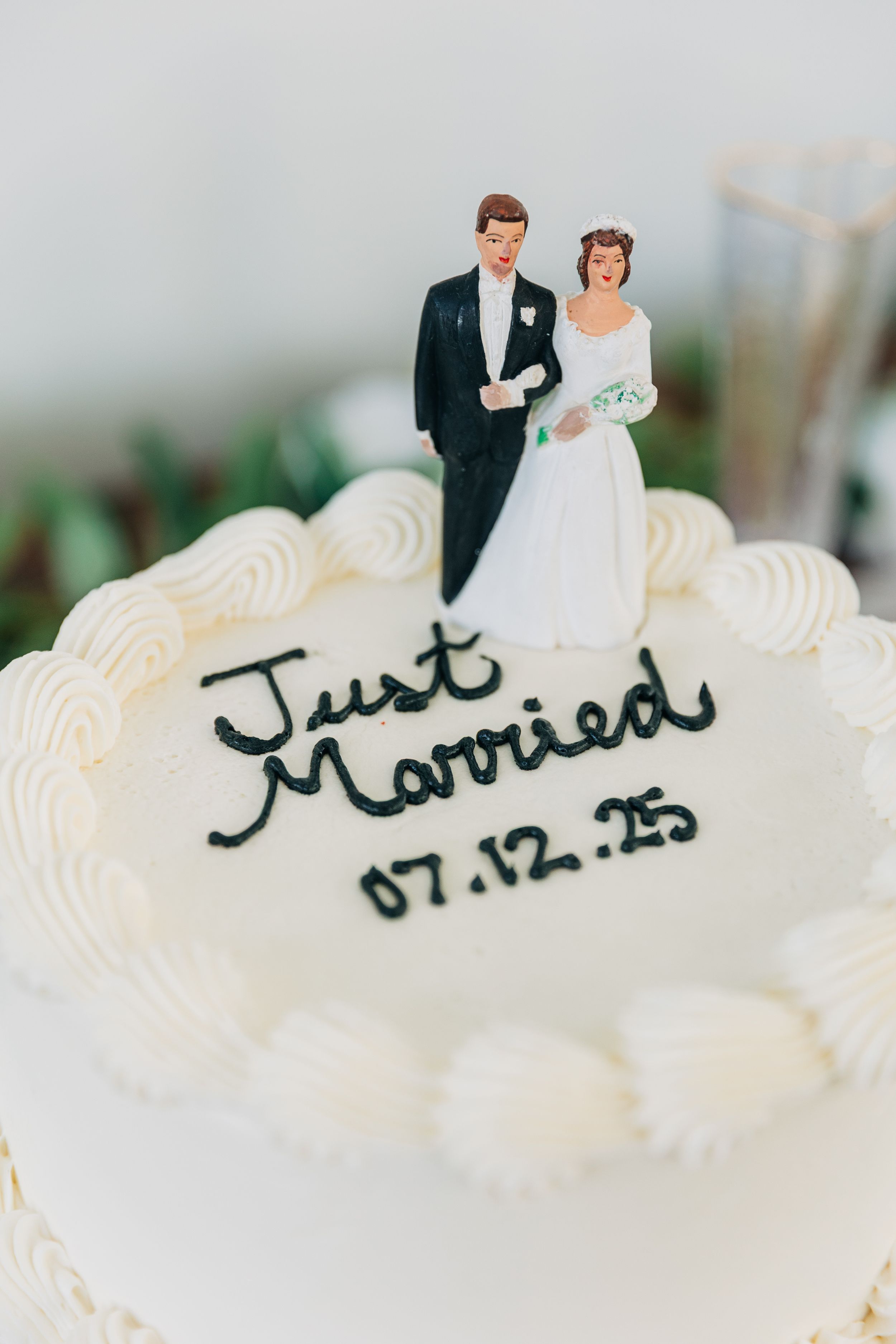 White frosted wedding cake with "Just Married" text and date written in black cursive script with a vintage bride and groom cake topper