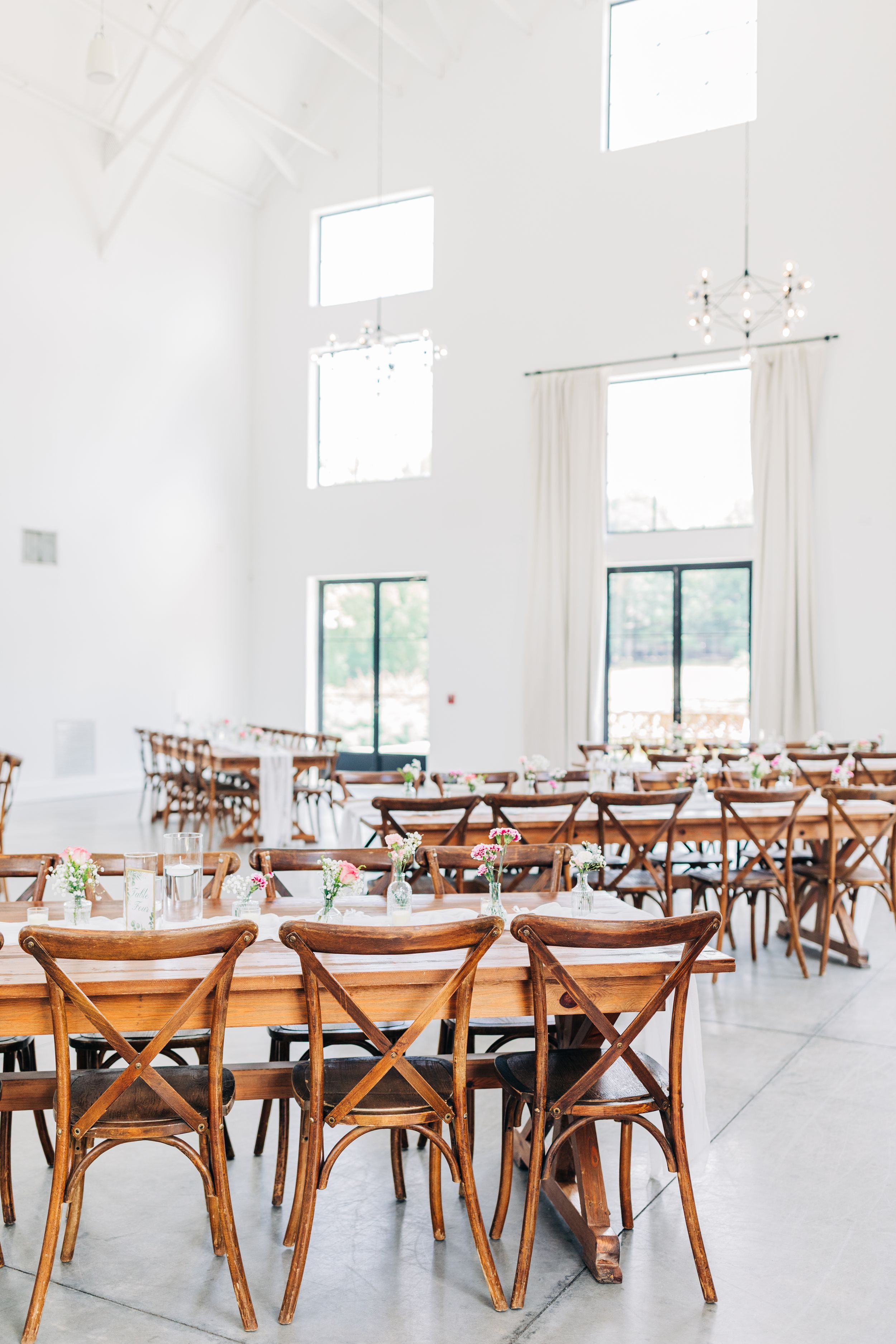 Light and airy wedding reception venue with rustic wooden cross-back chairs arranged in rows on white floors at Barn South
