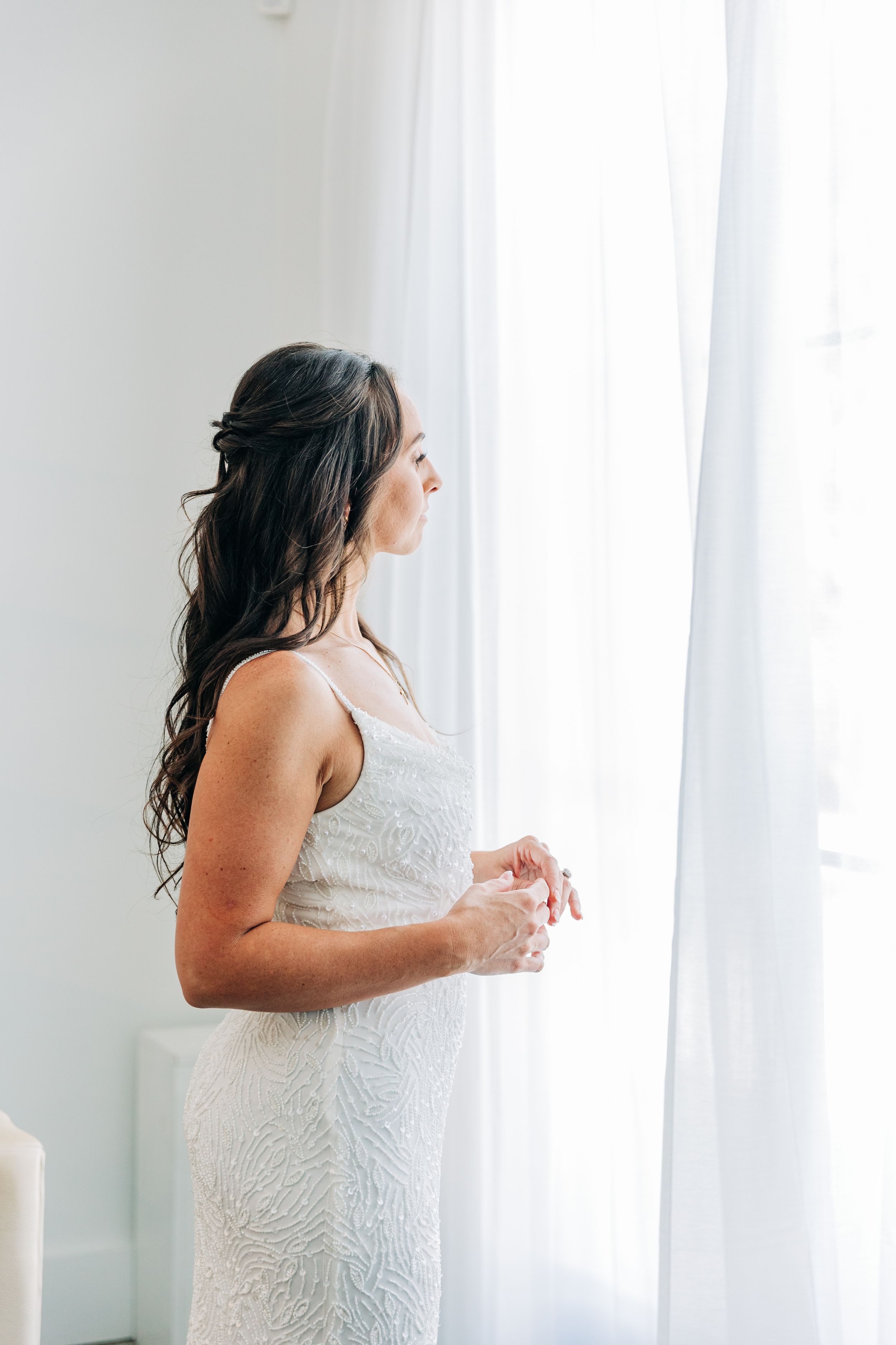 Bridal Portrait on her wedding dress standing by sheer white curtains before she's about to walk down the aisle