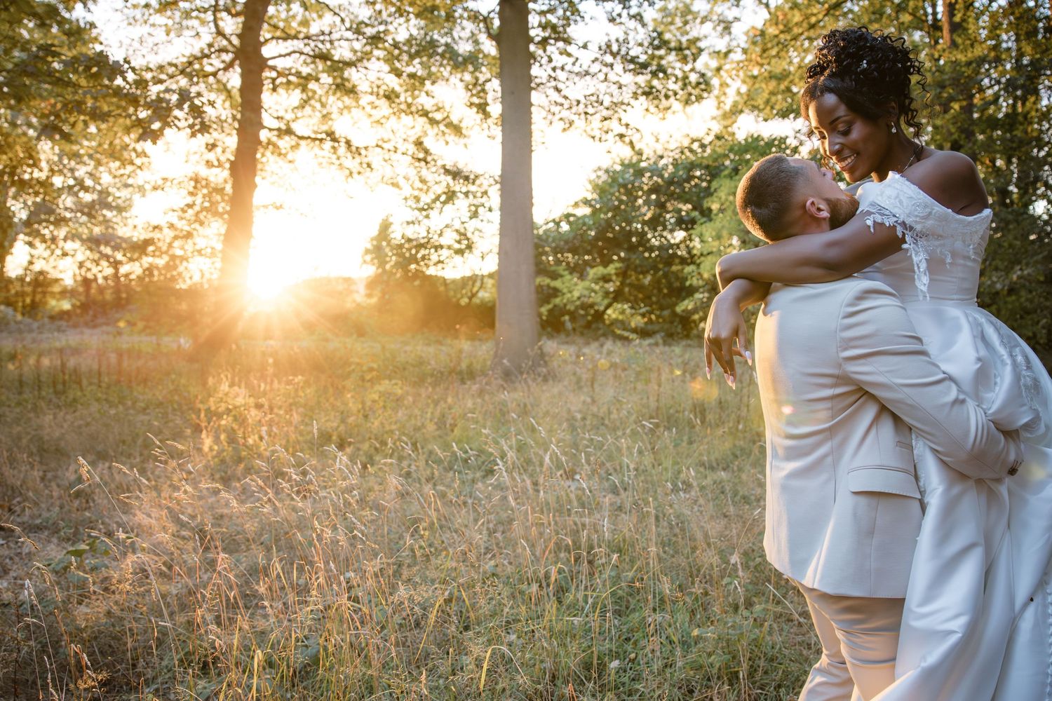 Bride and groom sharing an intimate embrace in a sunlit field at Kelham House during golden hour