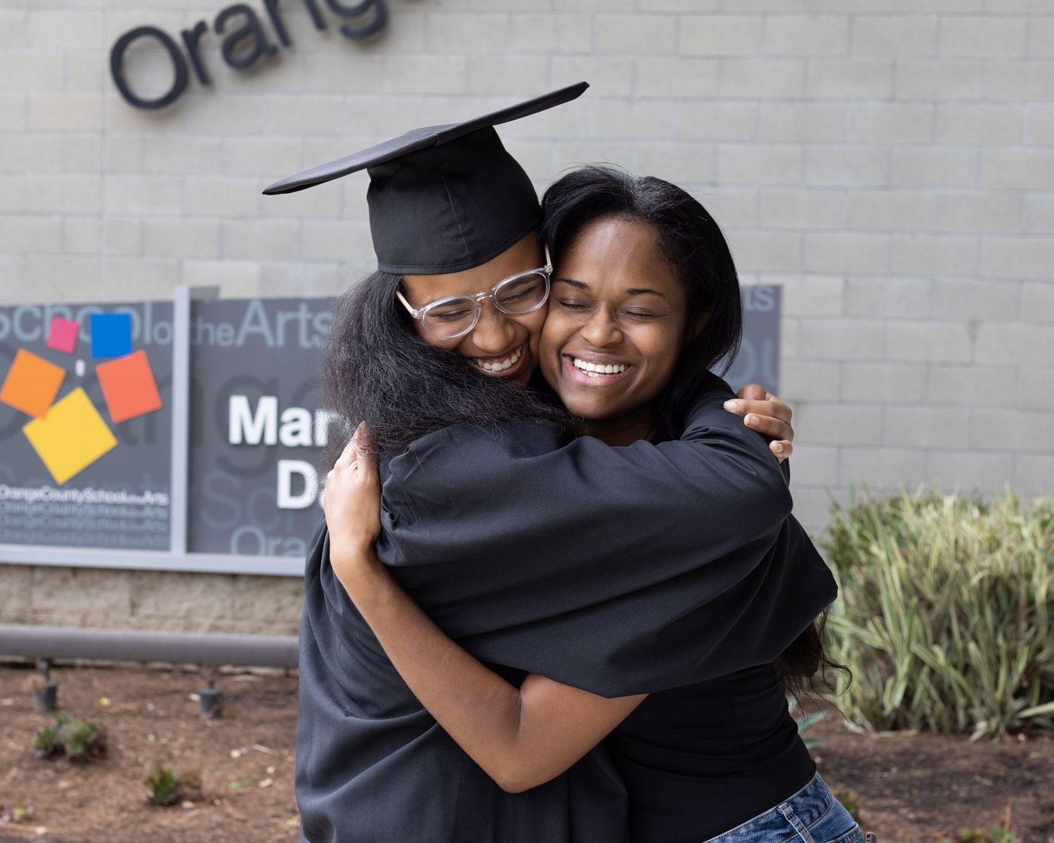 Mother and daughter share a warm embrace outside against a brick wall in a candid moment.