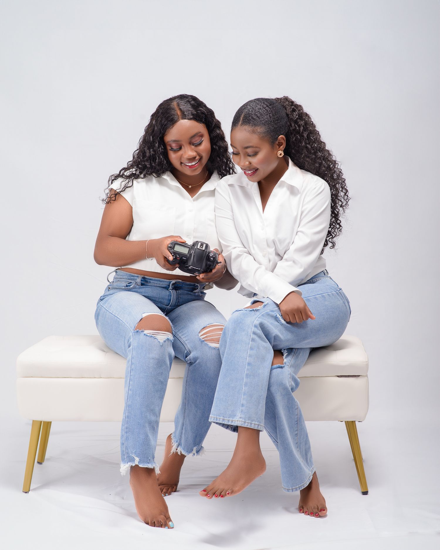 Two people in casual denim sit together on a white bench sharing a digital device.