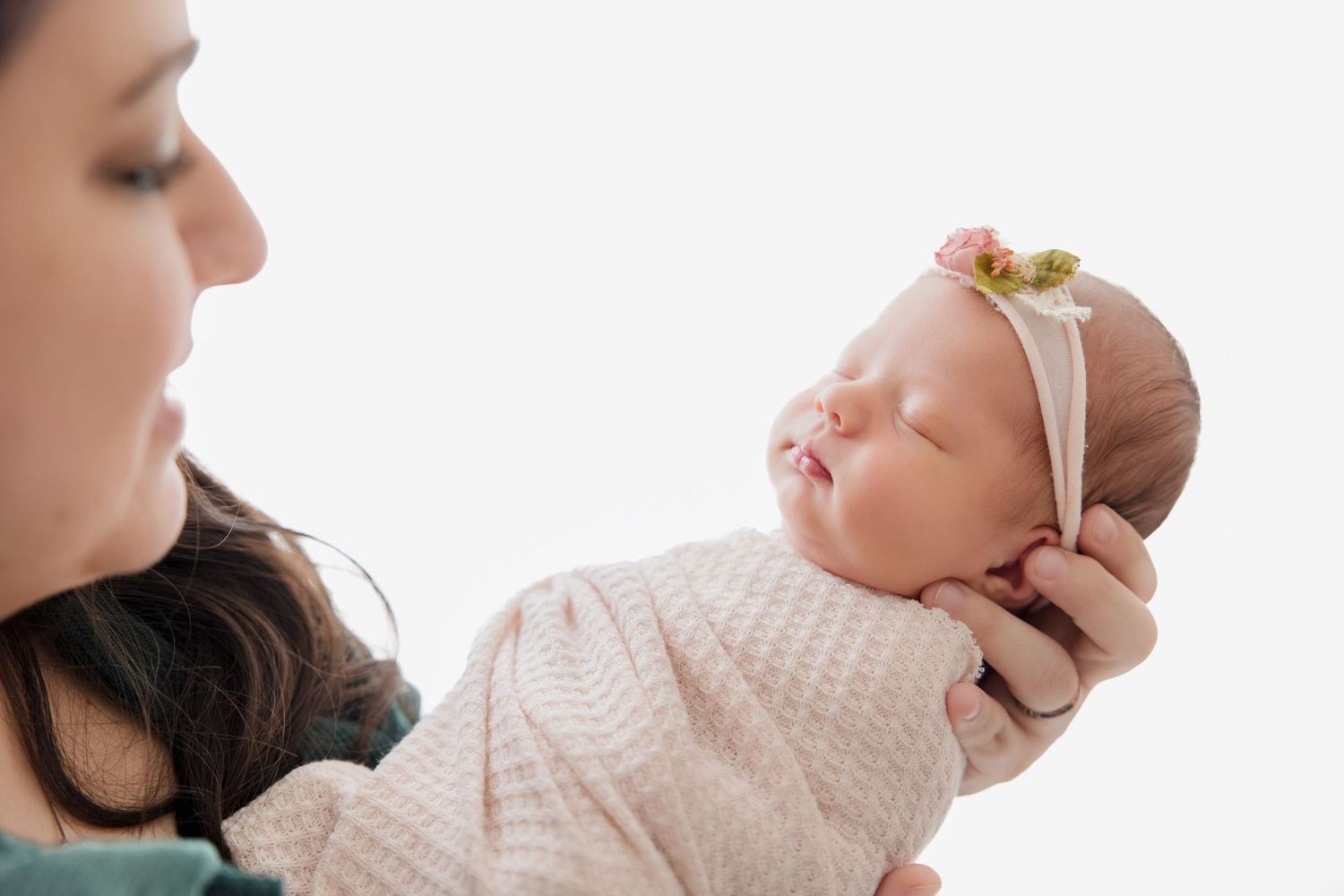 Delicate portraits of a sleeping newborn baby wearing white lace against a pink background.