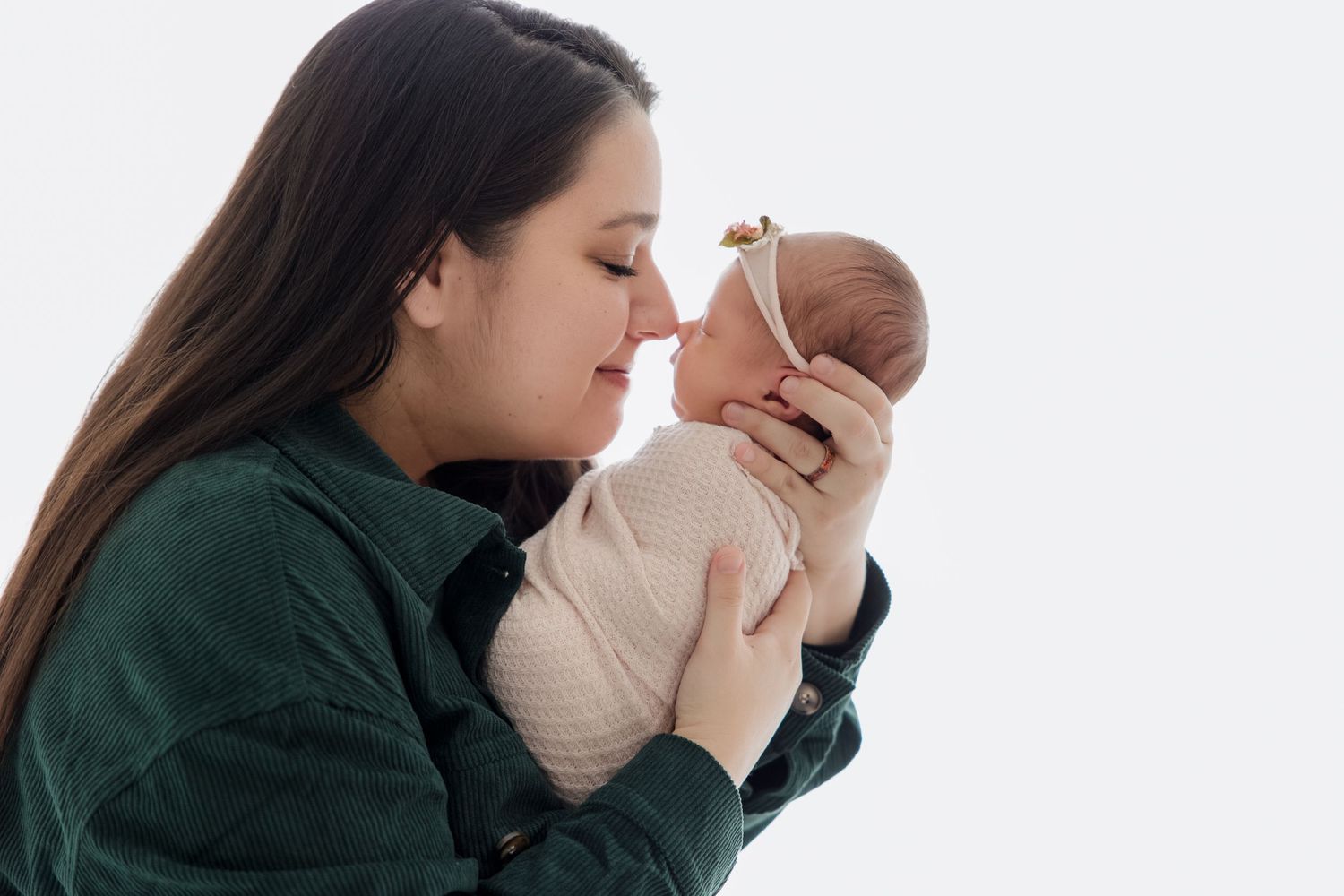 A tender moment showing someone cradling and kissing a newborn baby against a white backdrop.