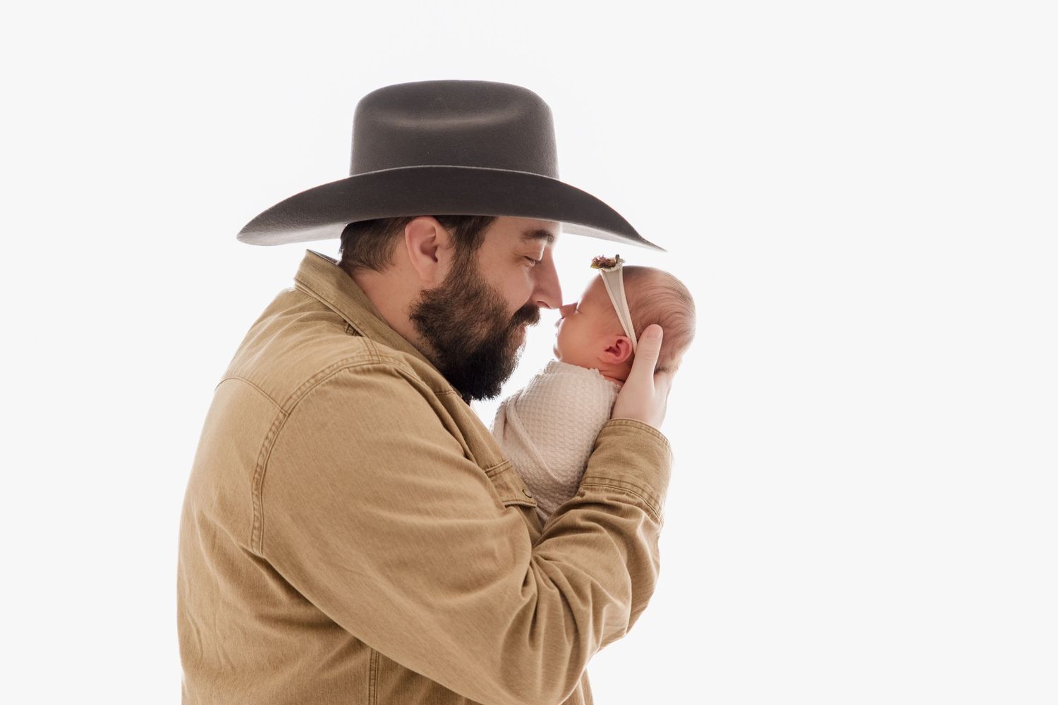 A cowboy adjusts his hat while wearing a tan shirt against a white background.
