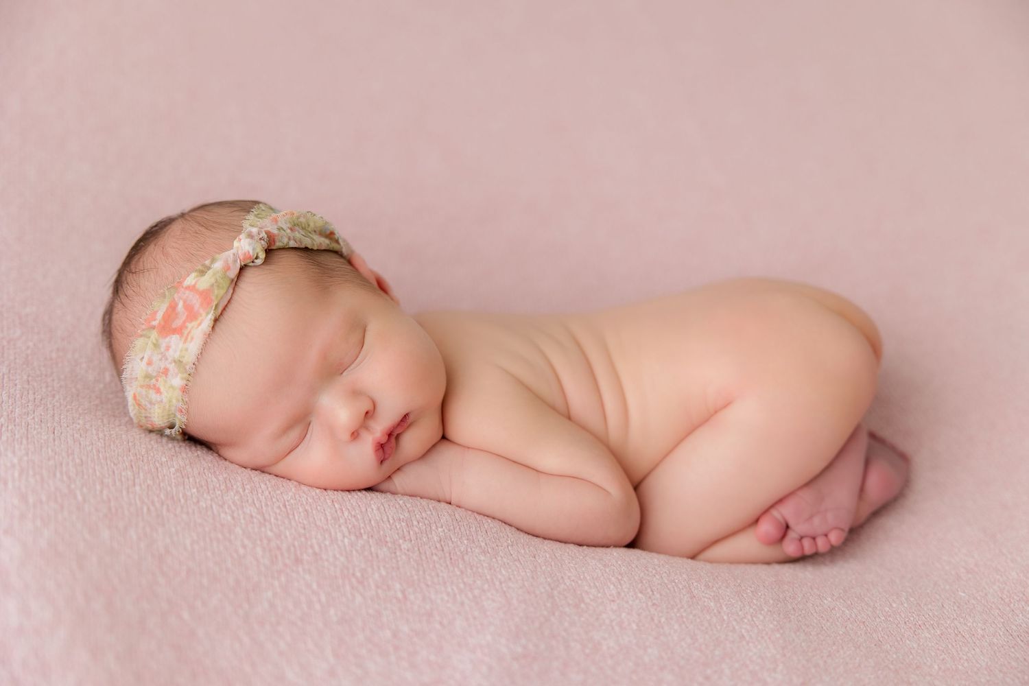 Sleeping newborn baby lying on soft pink blanket during professional photography session.
