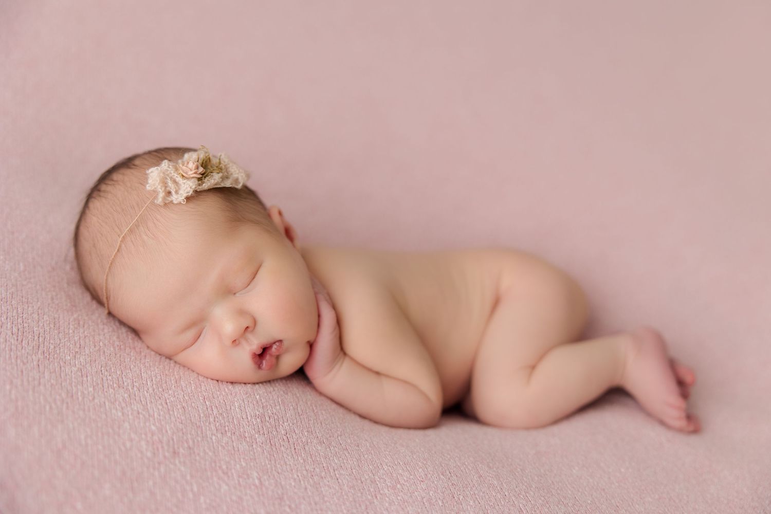 Peaceful sleeping newborn baby lying nude on soft pink fabric in artistic studio portrait pose.