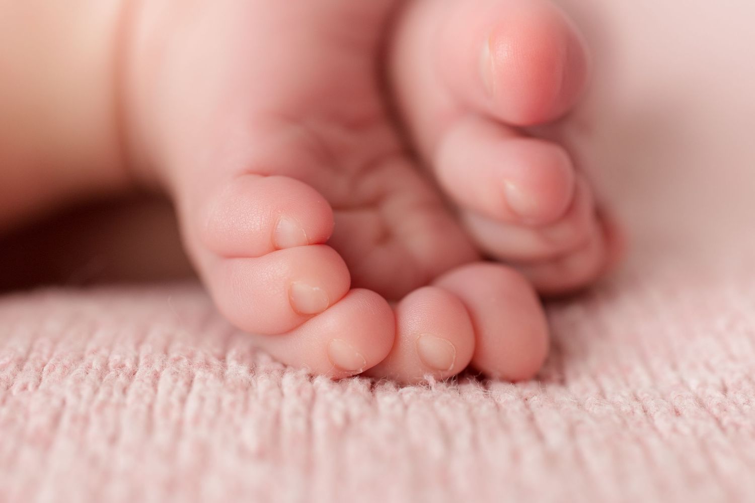 Macro shot of tiny newborn baby toes and feet against pink textured fabric.