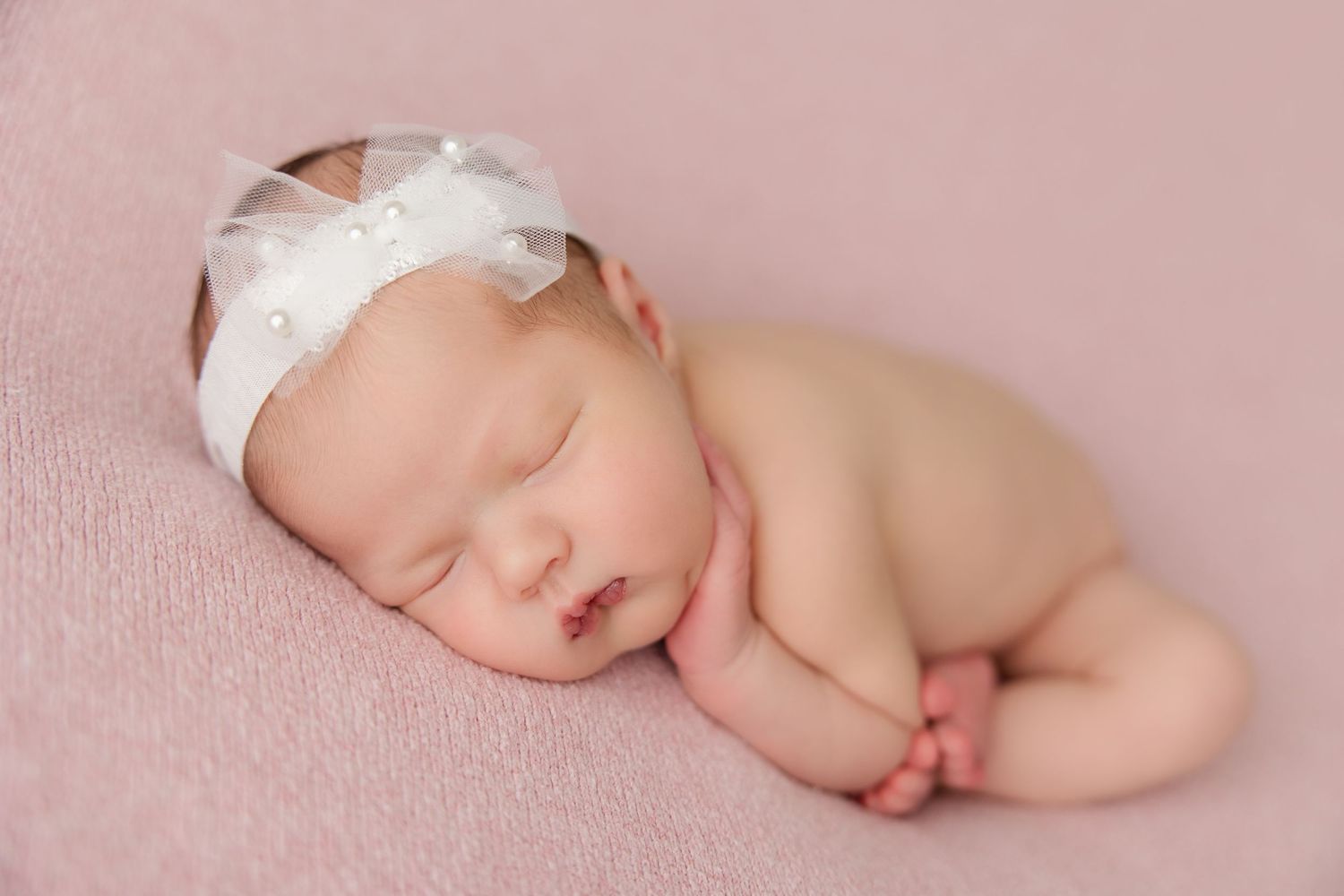 A series of peaceful newborn baby portraits against a soft pink backdrop with white bonnets and wraps.