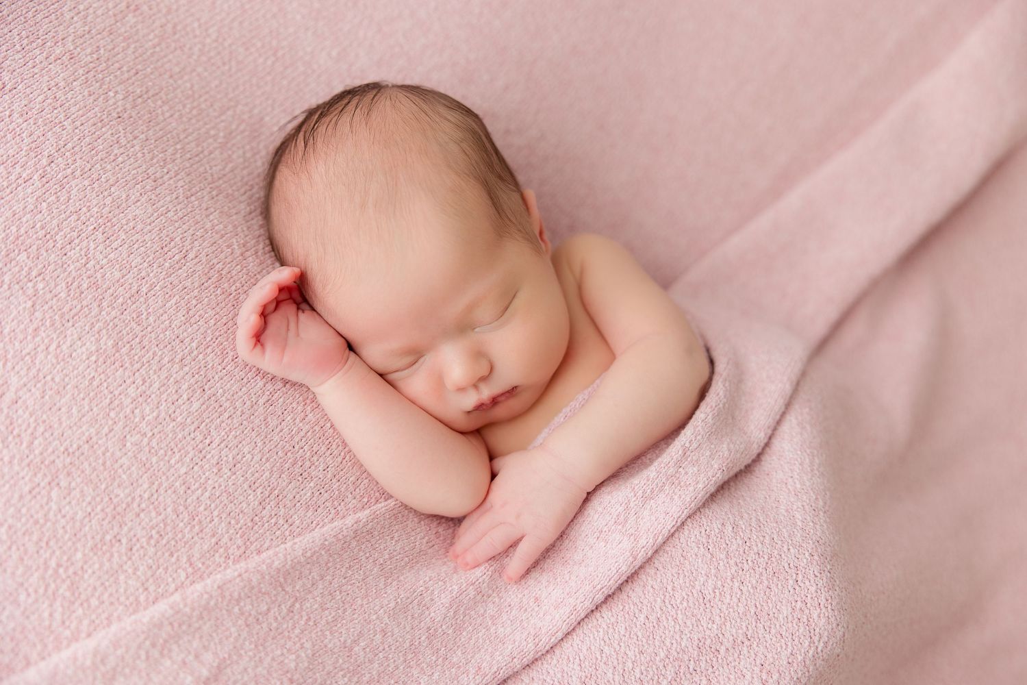 Professional studio portrait of sleeping newborn on soft pink textile background.