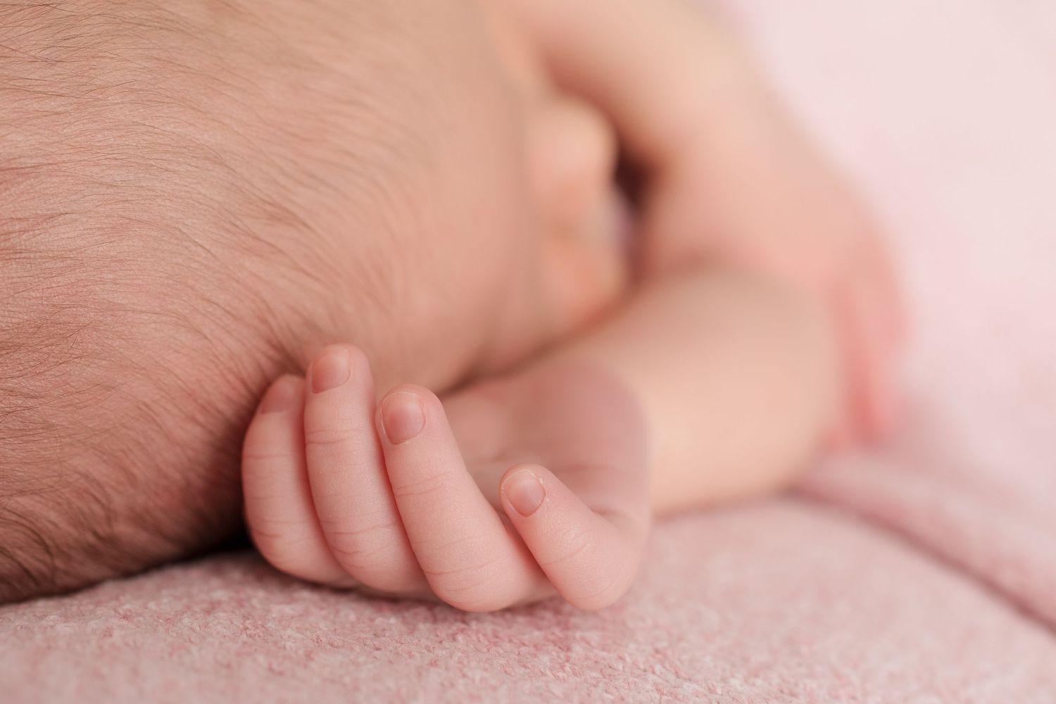 Delicate detail of a newborn's ear and soft skin against pink fabric in natural light.