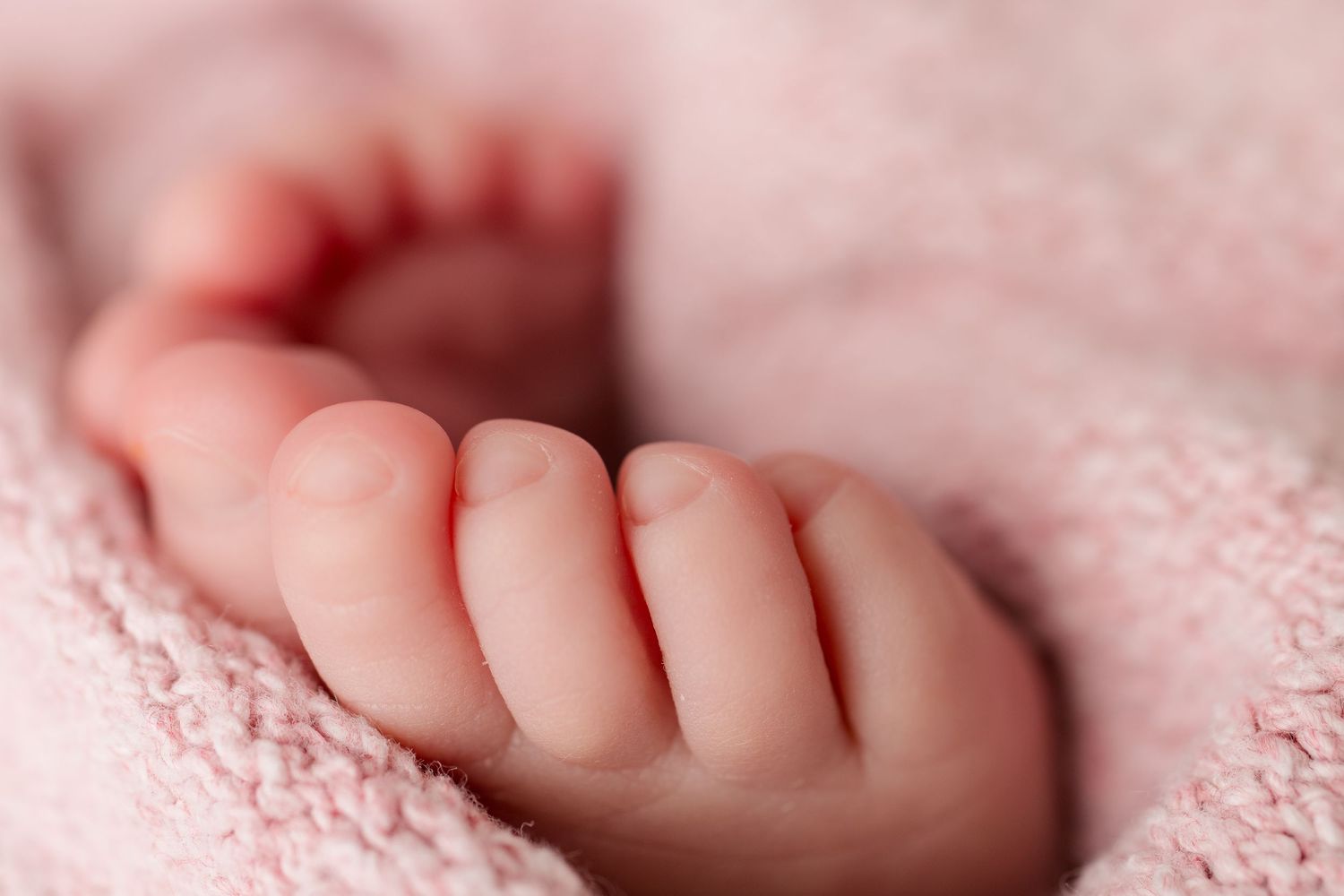 Close-up photo of tiny newborn fingers resting on pink textured fabric with gentle lighting.