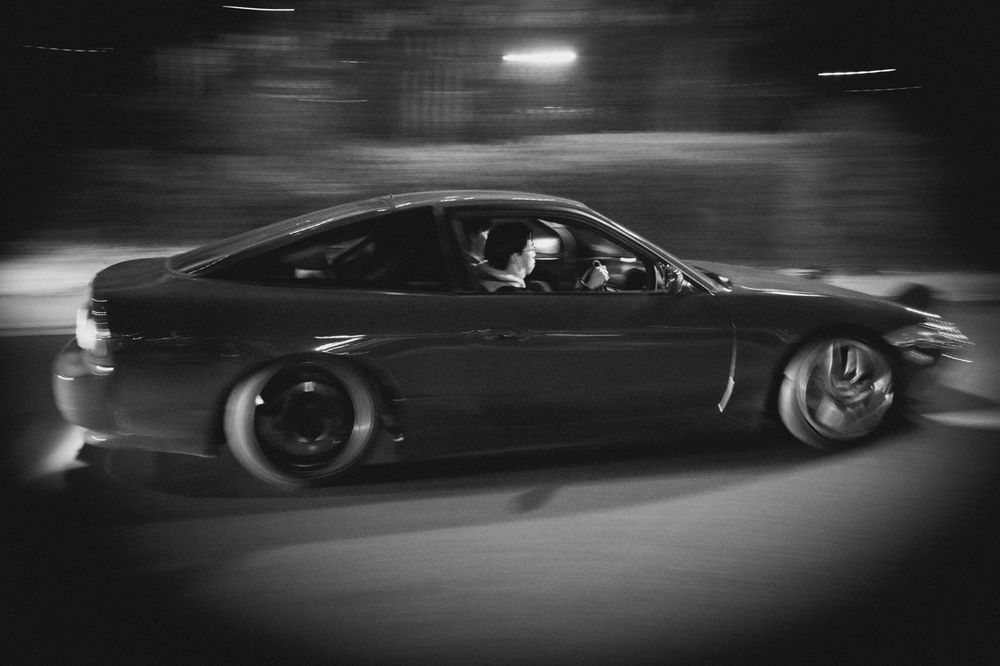 A blurred motion shot of a dark sports car racing at night, captured in black and white photography.