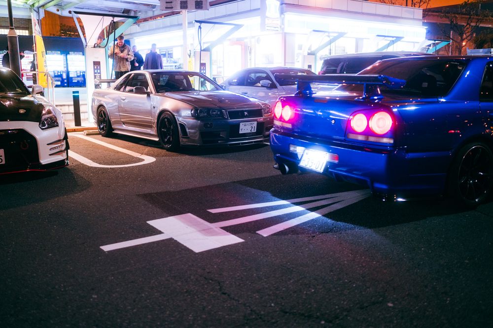Blue LED taillights illuminate multiple parked cars in a dimly lit parking lot at night.