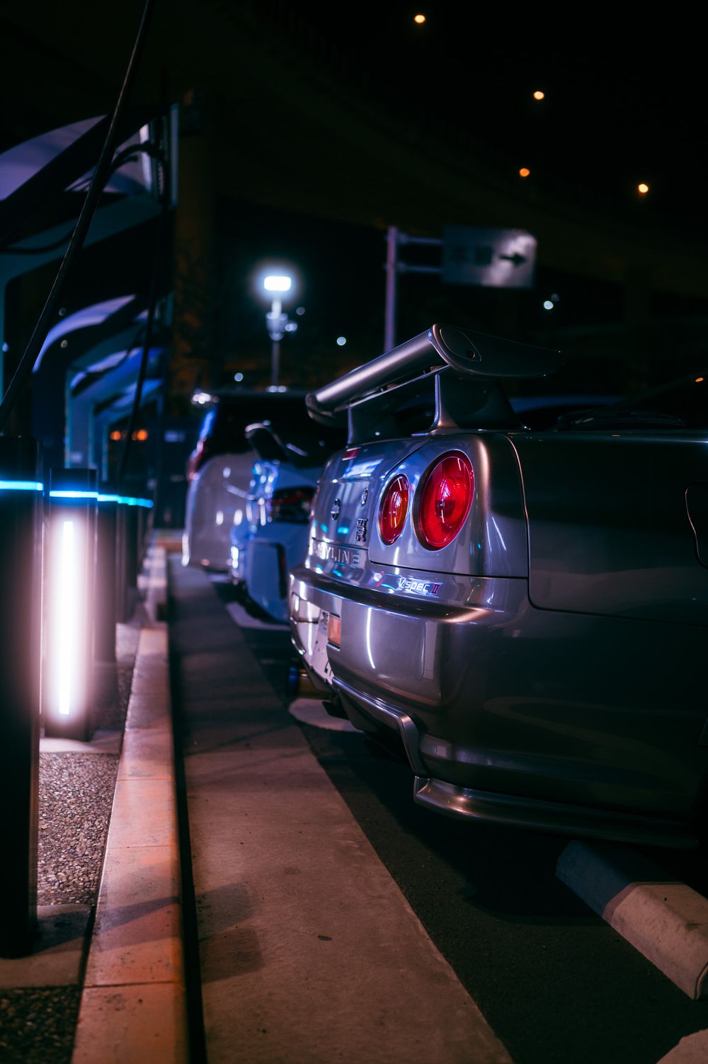 A line of parked cars at night illuminated by street lights and brake lights along a curb.