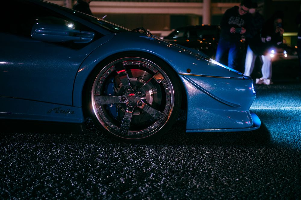 Purple and blue LED ground effects illuminate a modified sports car with custom wheels at night.
