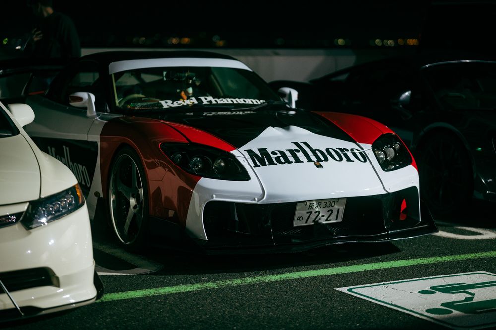 Six race cars from behind display their rear spoilers and engine components with different sponsor logos visible in low light.