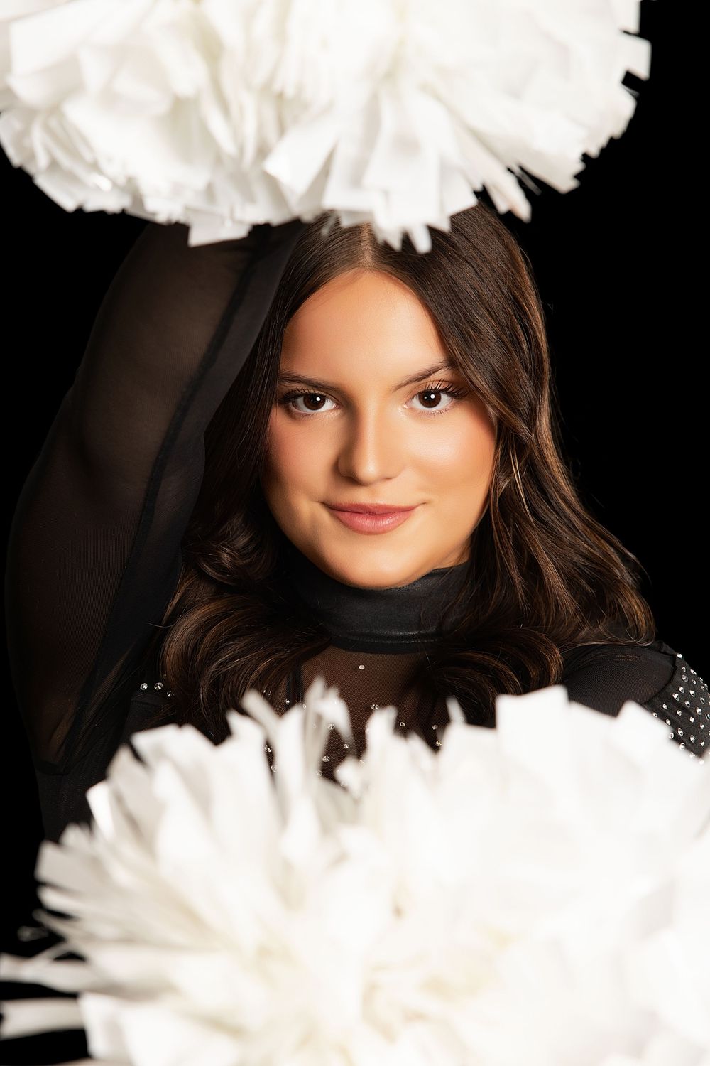 A cheerleader poses with white pom-poms against a black background, wearing a black uniform.