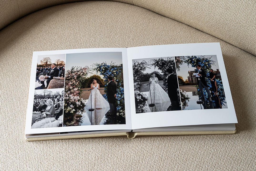 A wedding photo album lies open on a beige couch showing black and white ceremony photographs spread across its pages.