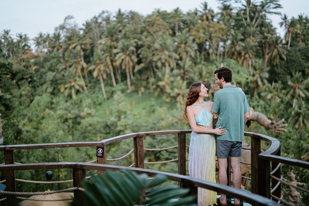 Couple enjoying sunset views from a wooden deck overlooking tropical valley.